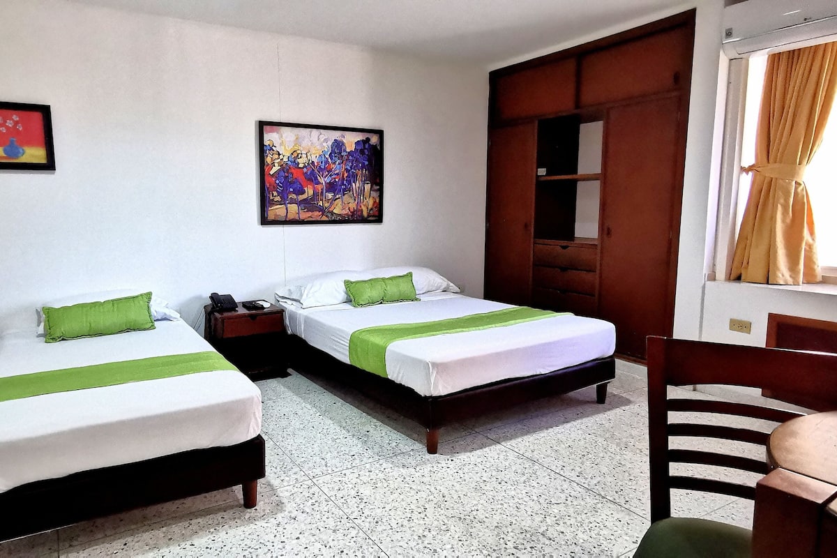 A room with two beds, a wooden chair, a table, and artwork on the walls.