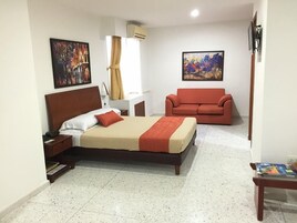A hotel room with a bed, a red sofa, a small table, and two paintings on the walls.