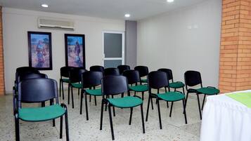 Un salón de conferencias con filas de sillas, una mesa blanca y dos cuadros en la pared.