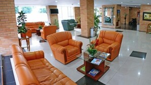 A lobby with orange leather sofas, a glass coffee table, and potted plants. - Hotel Torre del Prado (Barranquilla)