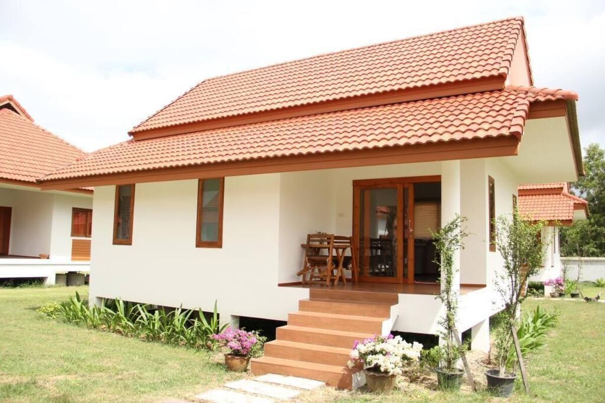 A two-story house with a red-tiled roof, a front porch with a wooden bench, and a small garden with potted plants.