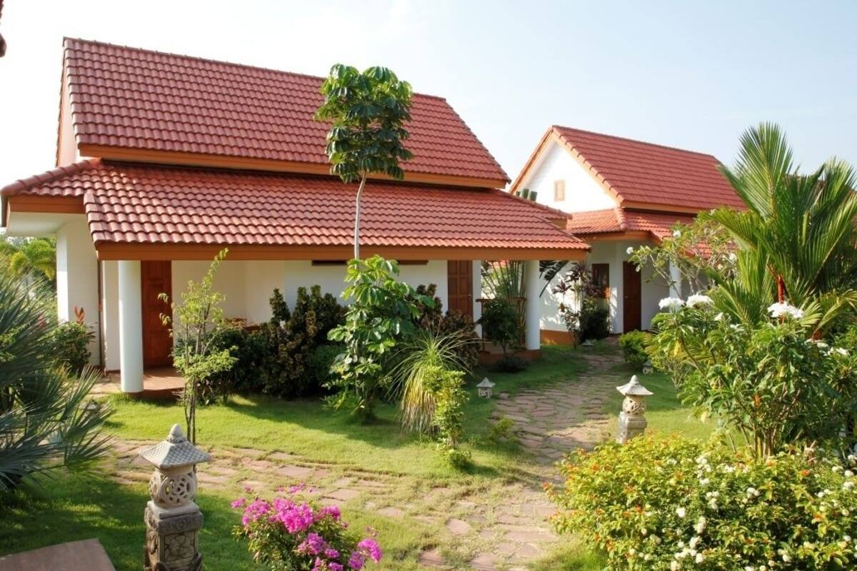 A two-story building with a red-tiled roof, surrounded by a well-maintained garden with various plants and a stone pathway.