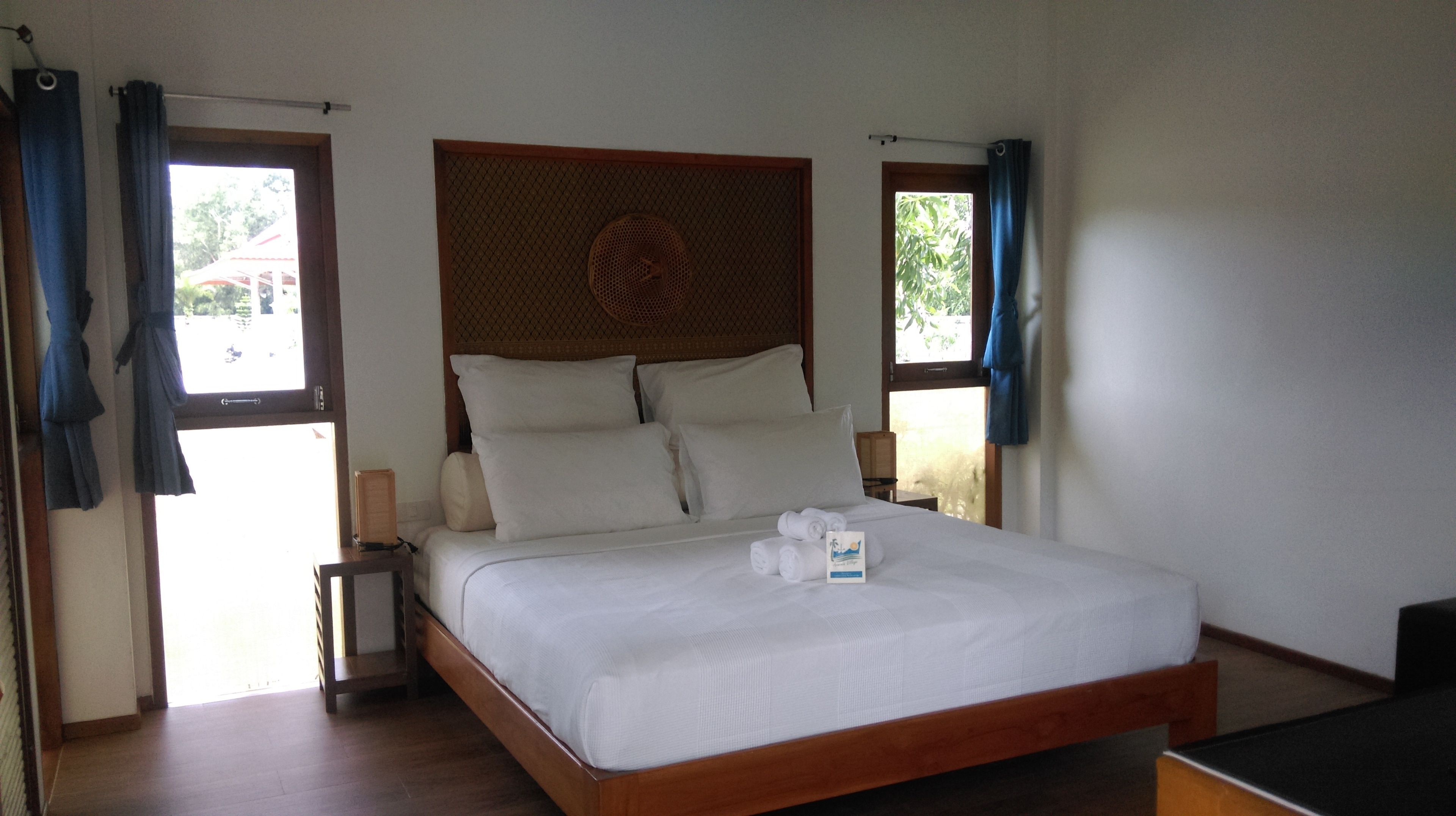 Una cama bien hecha con sábanas y almohadas blancas, un cabecero de madera y una mesita de noche con una lámpara.