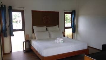 Una cama bien hecha con sábanas y almohadas blancas, un cabecero de madera y una mesita de noche con una lámpara.