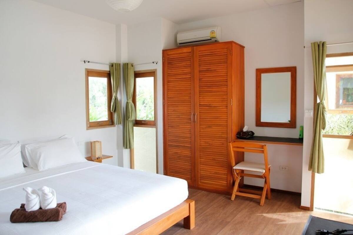 A bedroom with a bed, wooden wardrobe, desk, chair, and a mirror.