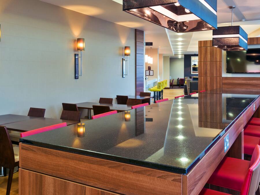 A modern hotel lobby with a long bar, wooden furniture, and contemporary lighting fixtures.