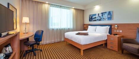 A hotel room with a bed, a desk with a chair, a television, a lamp, a nightstand, and a wall painting.