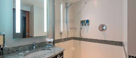 A modern bathroom with a granite countertop, a large mirror, a shower with a glass door, and a tiled floor.