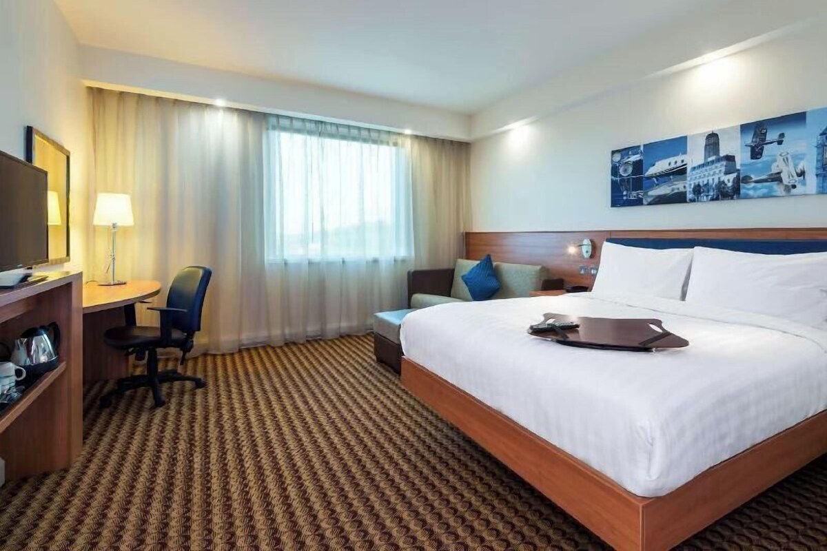 A hotel room with a large bed, a desk with a chair, a television, and a painting on the wall.