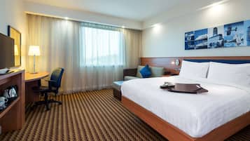 A hotel room with a large bed, a desk with a chair, a television, and a painting on the wall.