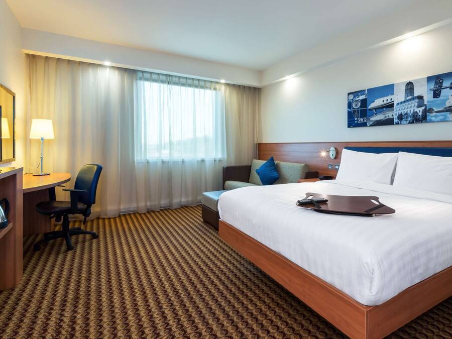 A hotel room with a large bed, a desk with a chair, a television, and a painting on the wall.