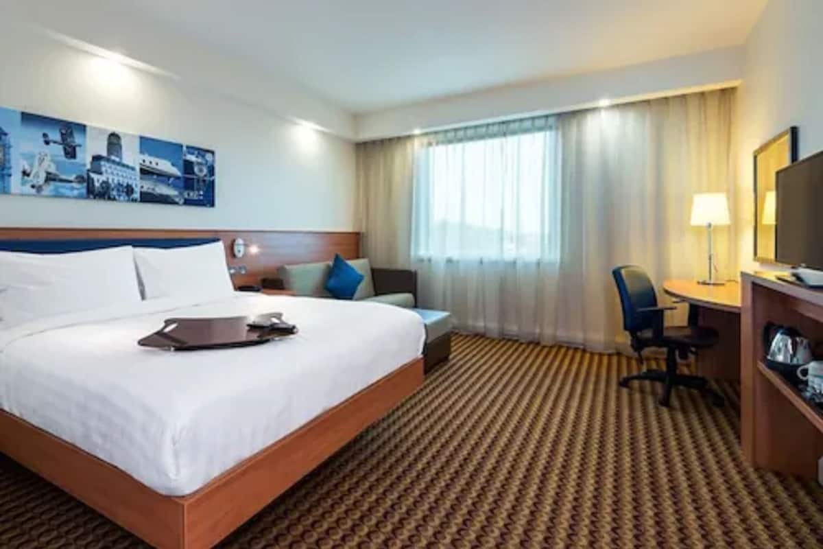 A hotel room with a large bed, a desk with a chair, a television, and a window with curtains.