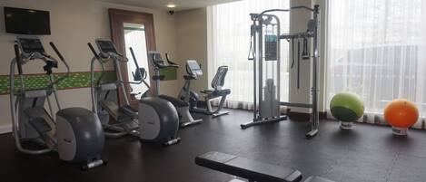 Un gimnasio con diversos equipos de ejercicio, incluyendo cintas de correr, elípticas, una prensa de banca y pesas libres.