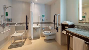 A modern bathroom with a shower, toilet, and sink, equipped with accessibility features like grab bars and a wheelchair-accessible shower chair.