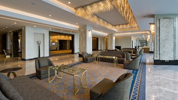 Un hall d’entrée spacieux avec un plafond haut, un tapis à motifs et un mobilier moderne comprenant des canapés et une table basse en verre.