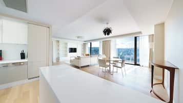 Una cocina moderna con muebles blancos, un comedor con mesa y sillas blancas, y un amplio ventanal con vistas a la ciudad.