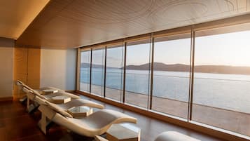 Una stanza moderna con un'ampia finestra vista su un lago e delle colline, dotata di poltrone massaggianti e soffitto in legno.