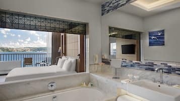Habitación de hotel con una cama grande, una bañera, un tocador con espejo y vista al mar.