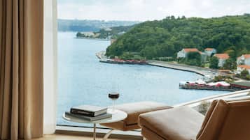 Une chambre avec vue sur une rivière, un verre de vin et un livre posé sur une petite table.