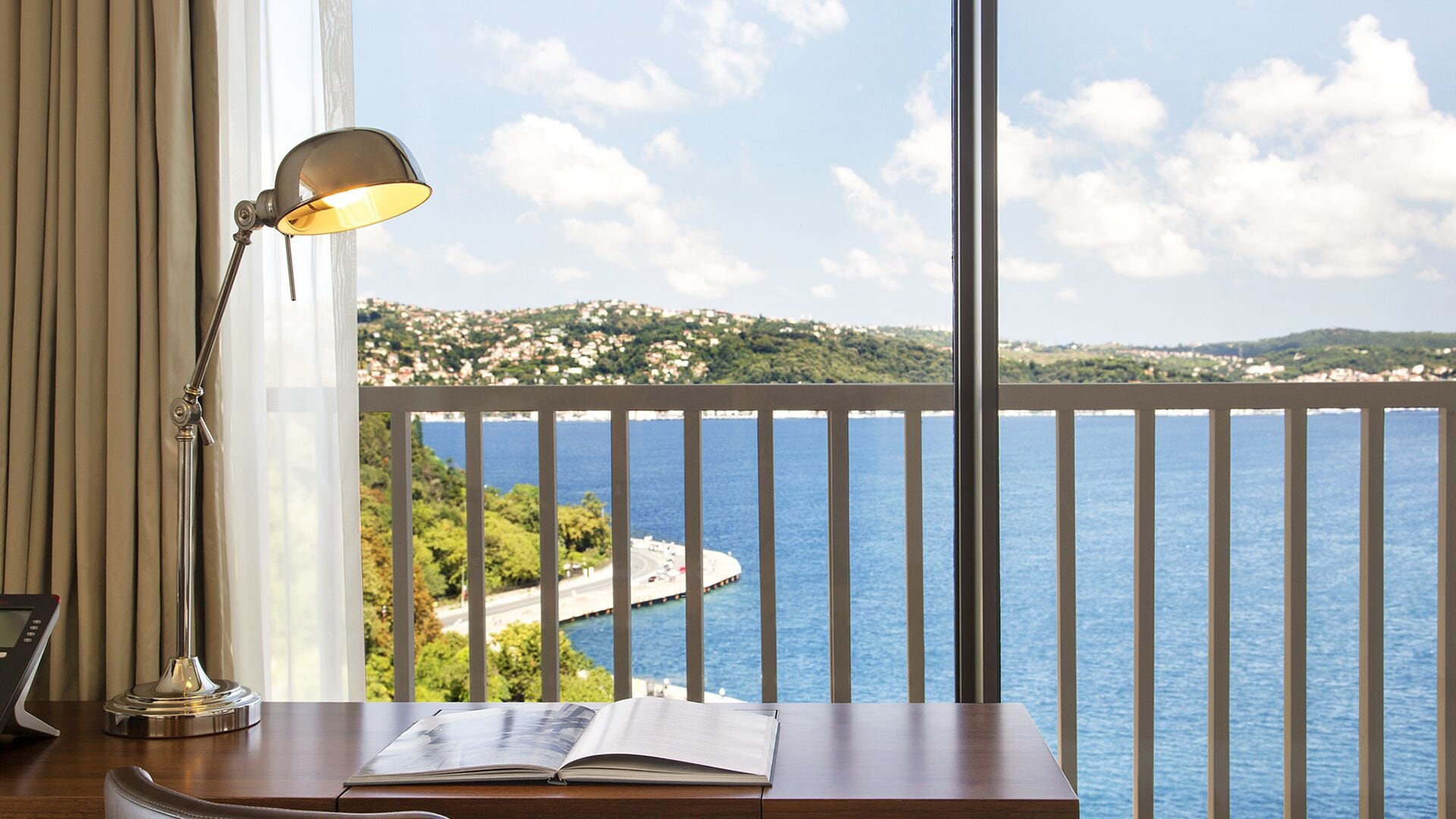 Une pièce avec un bureau, une lampe et une vue sur un paysage côtier.
