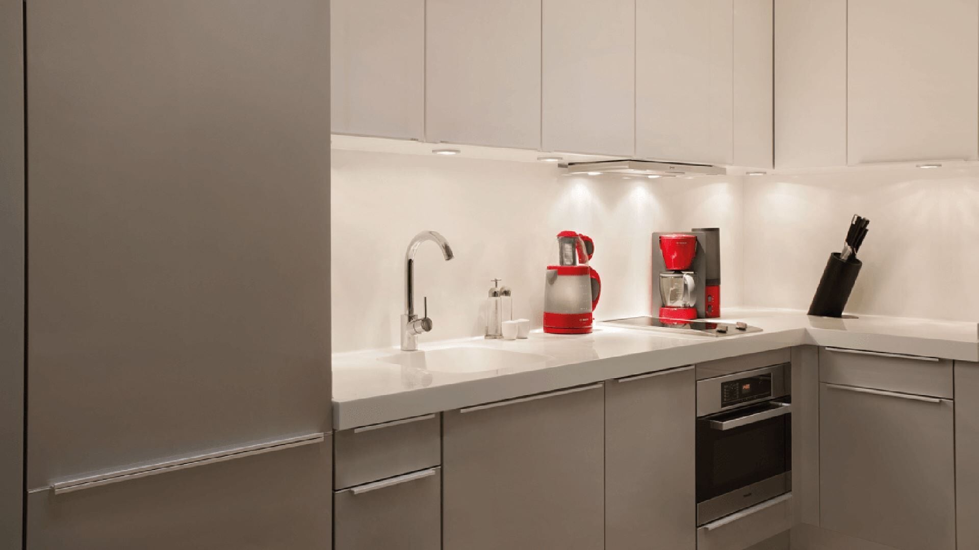 Una cucina moderna con un piano di lavoro bianco, elettrodomestici in acciaio inossidabile, una macchina da caffè rossa e un portacoltelli.