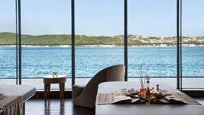A room with a large window overlooking a body of water and a distant coastline. There is a bed, a chair, and a small table with a tray of condiments. - The Grand Tarabya Managed by Accor (Sariyer)