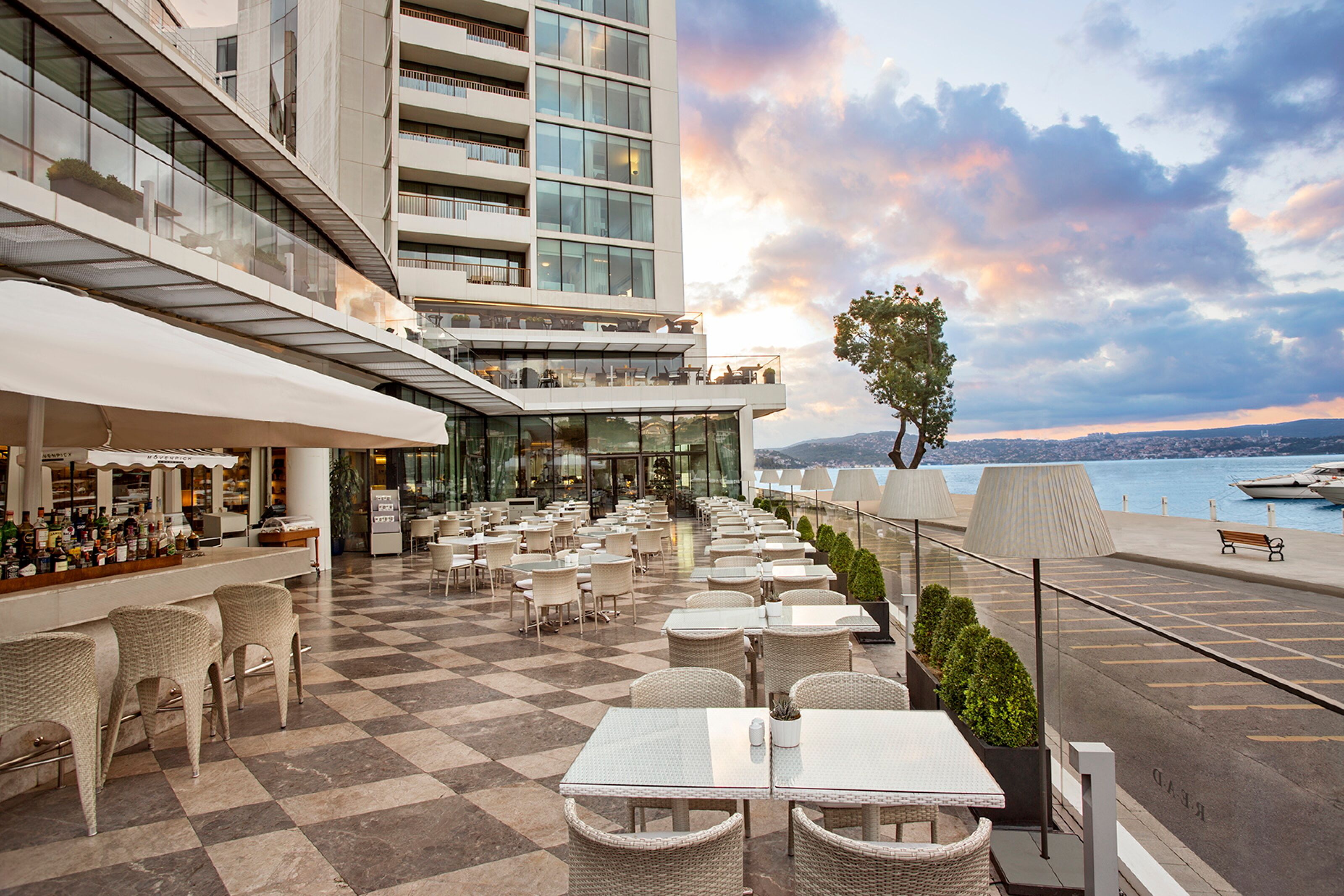 A rooftop terrace with checkered flooring, outdoor seating, and a view of the water.