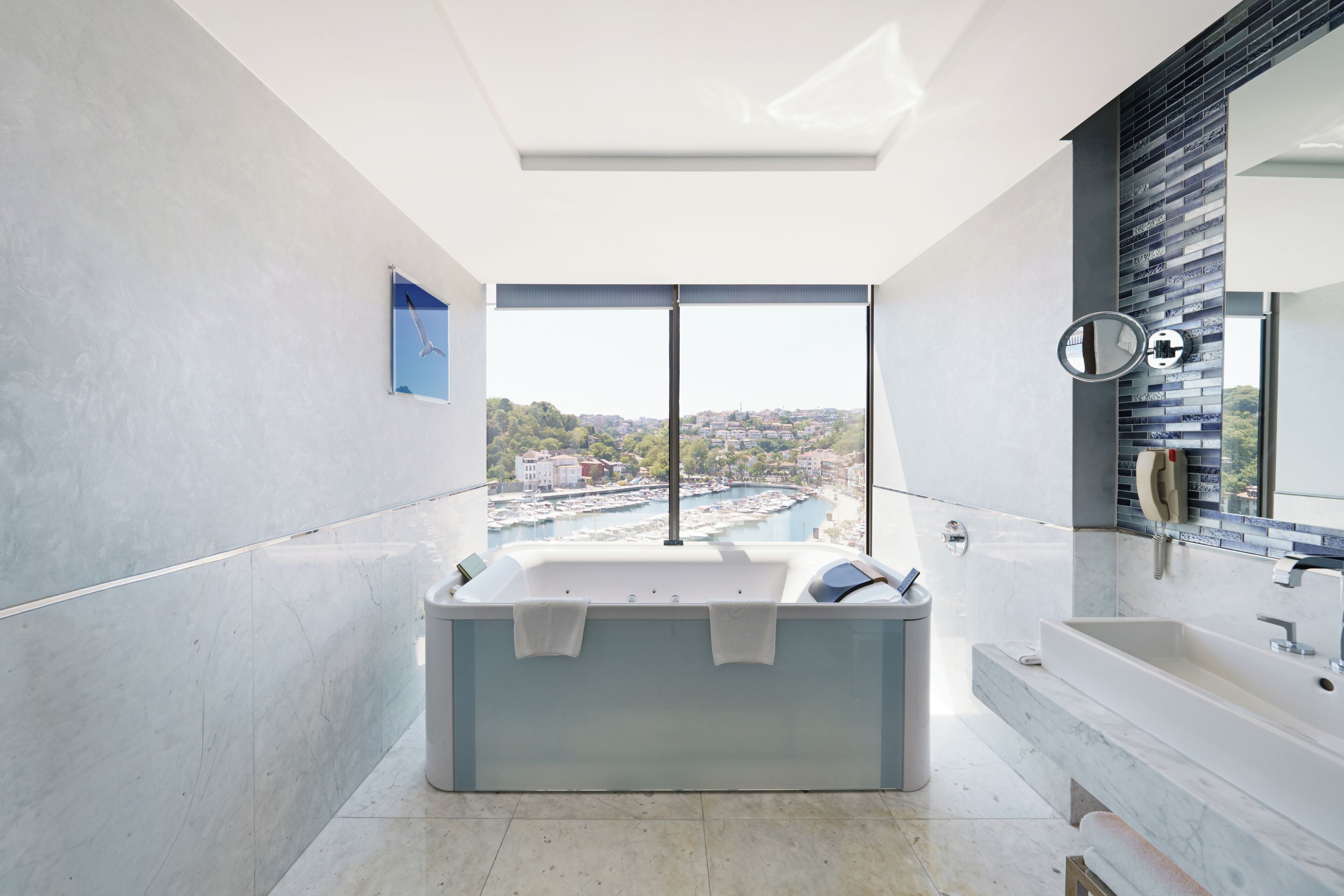 A modern bathroom with a large bathtub, a separate sink, and a view of a marina.