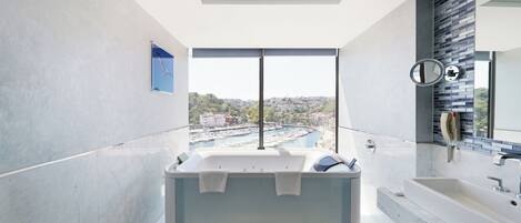 A modern bathroom with a large bathtub, a separate sink, and a view of a marina.
