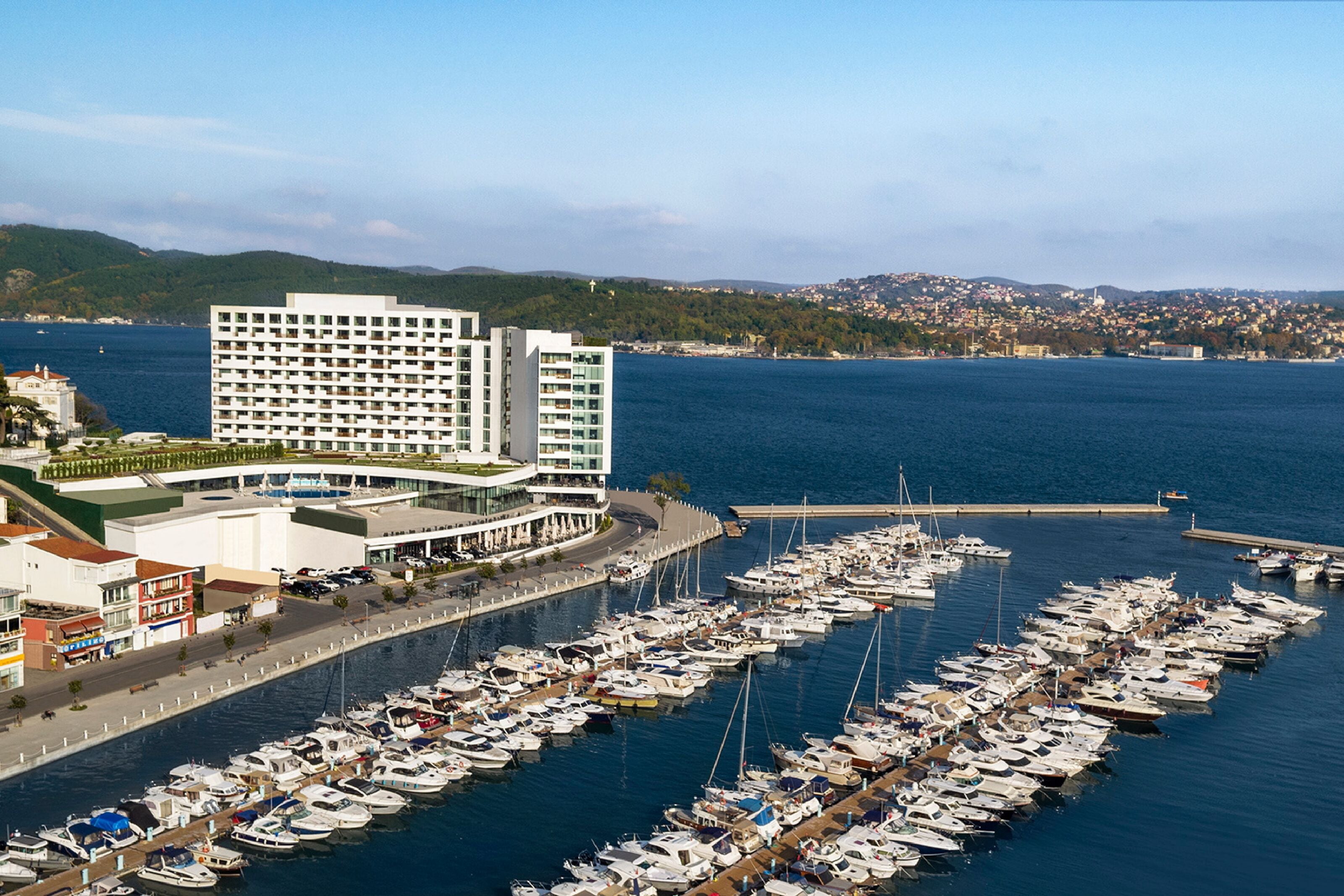 Un puerto deportivo con numerosas embarcaciones amarradas, un gran edificio de hotel y un paisaje urbano al fondo.