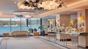 Amplia habitación con vista al mar, mesa de desayuno buffet con diversos alimentos y una lámpara de techo original.