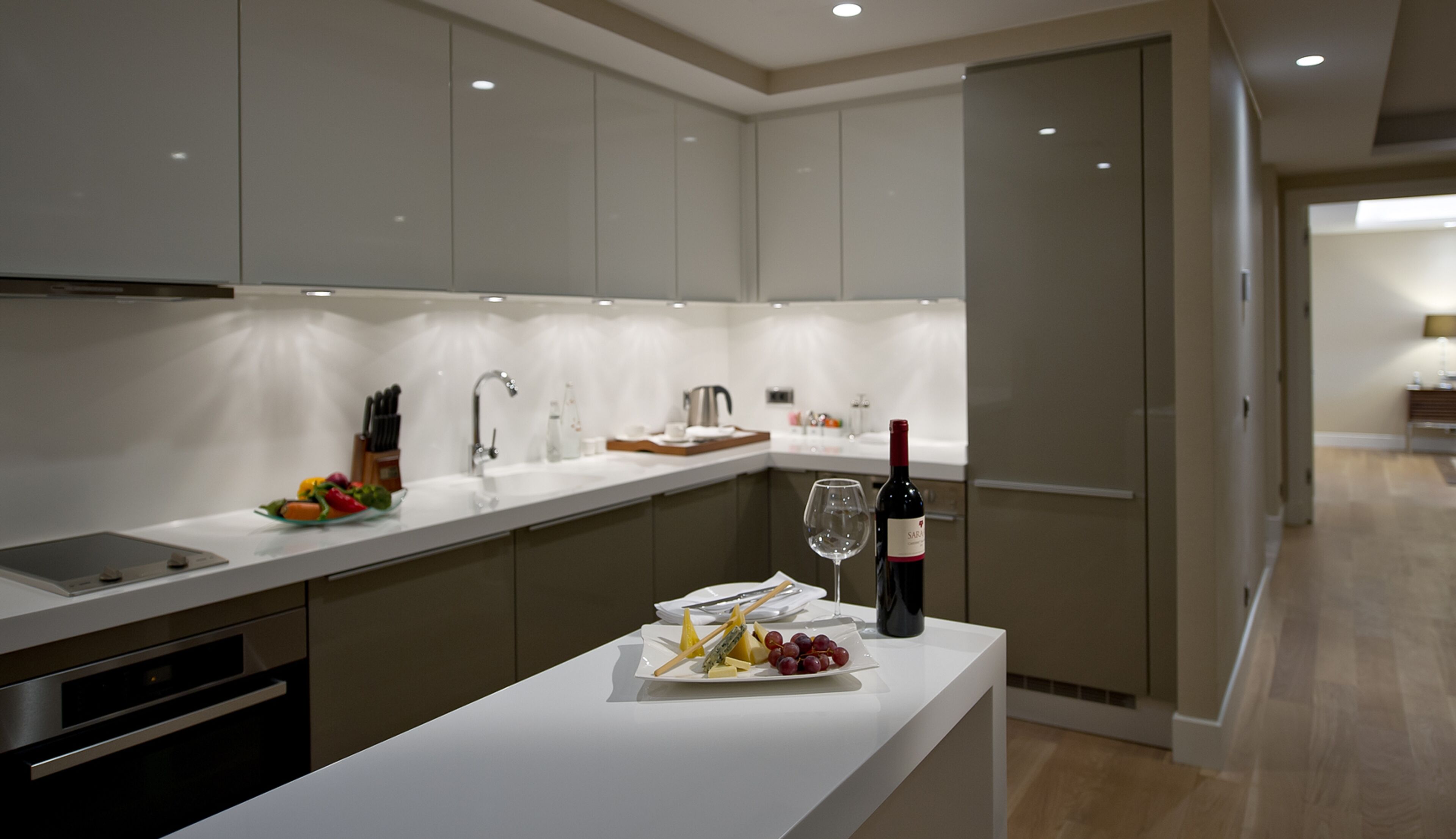 Una cocina moderna con armarios blancos, electrodomésticos de acero inoxidable y una isla central con una botella de vino y fruta.