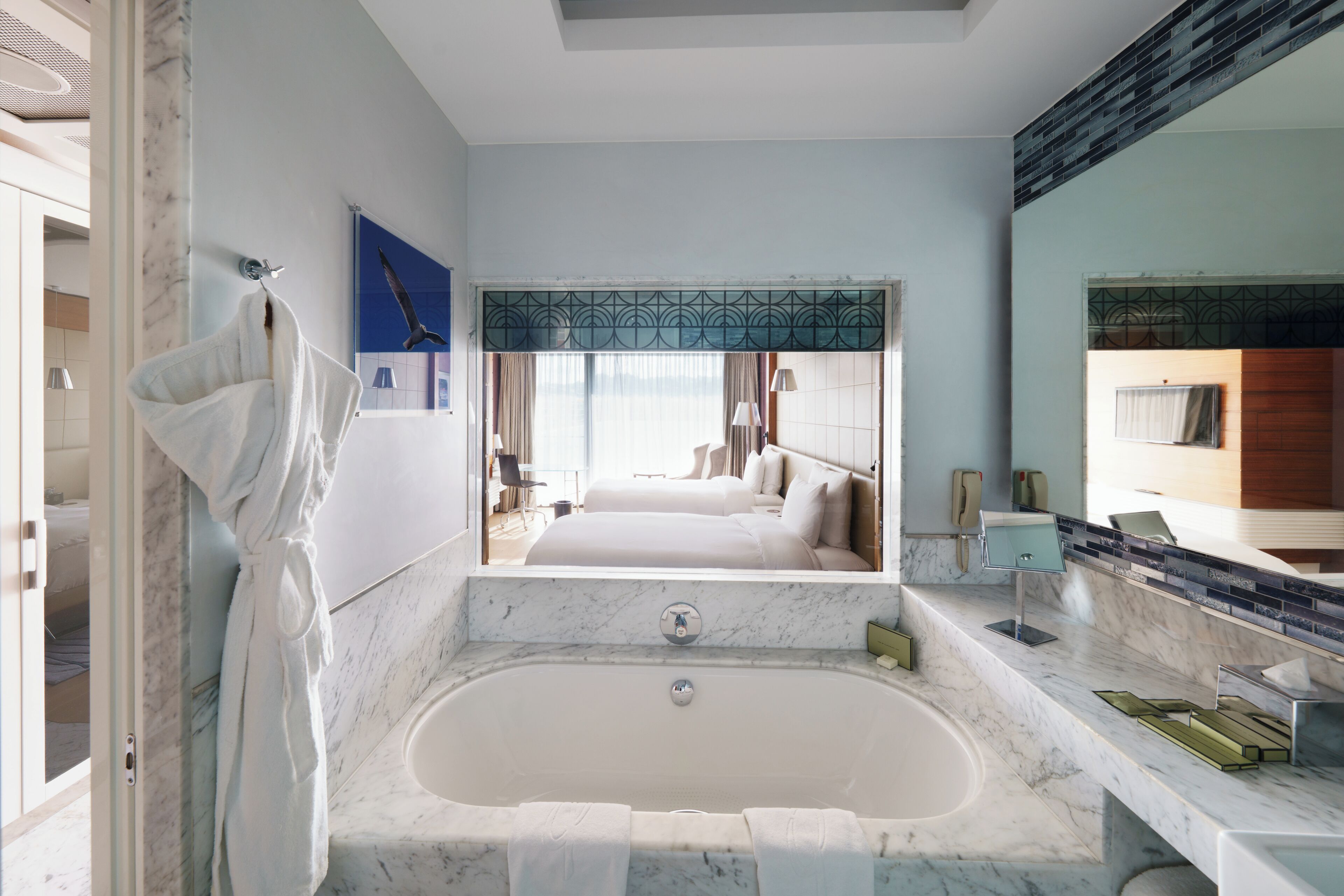 Un bagno moderno con una vasca da bagno ampia, uno specchio e vista su una camera da letto.