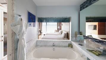 Une salle de bain moderne avec une grande baignoire, un miroir et une vue sur la chambre.