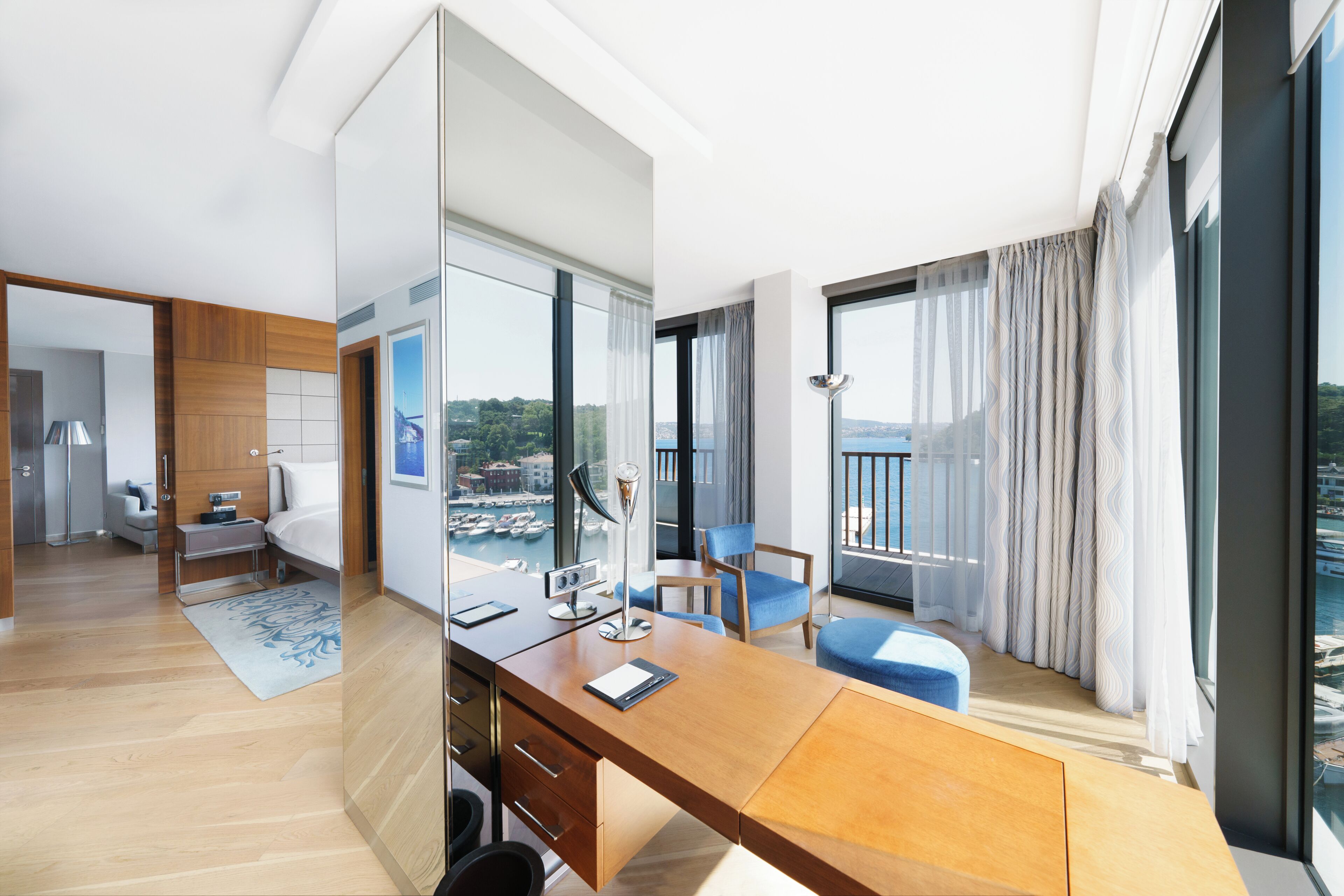 Camera d'albergo moderna con una scrivania in legno, una sedia, un letto, uno specchio grande e vista sul mare.