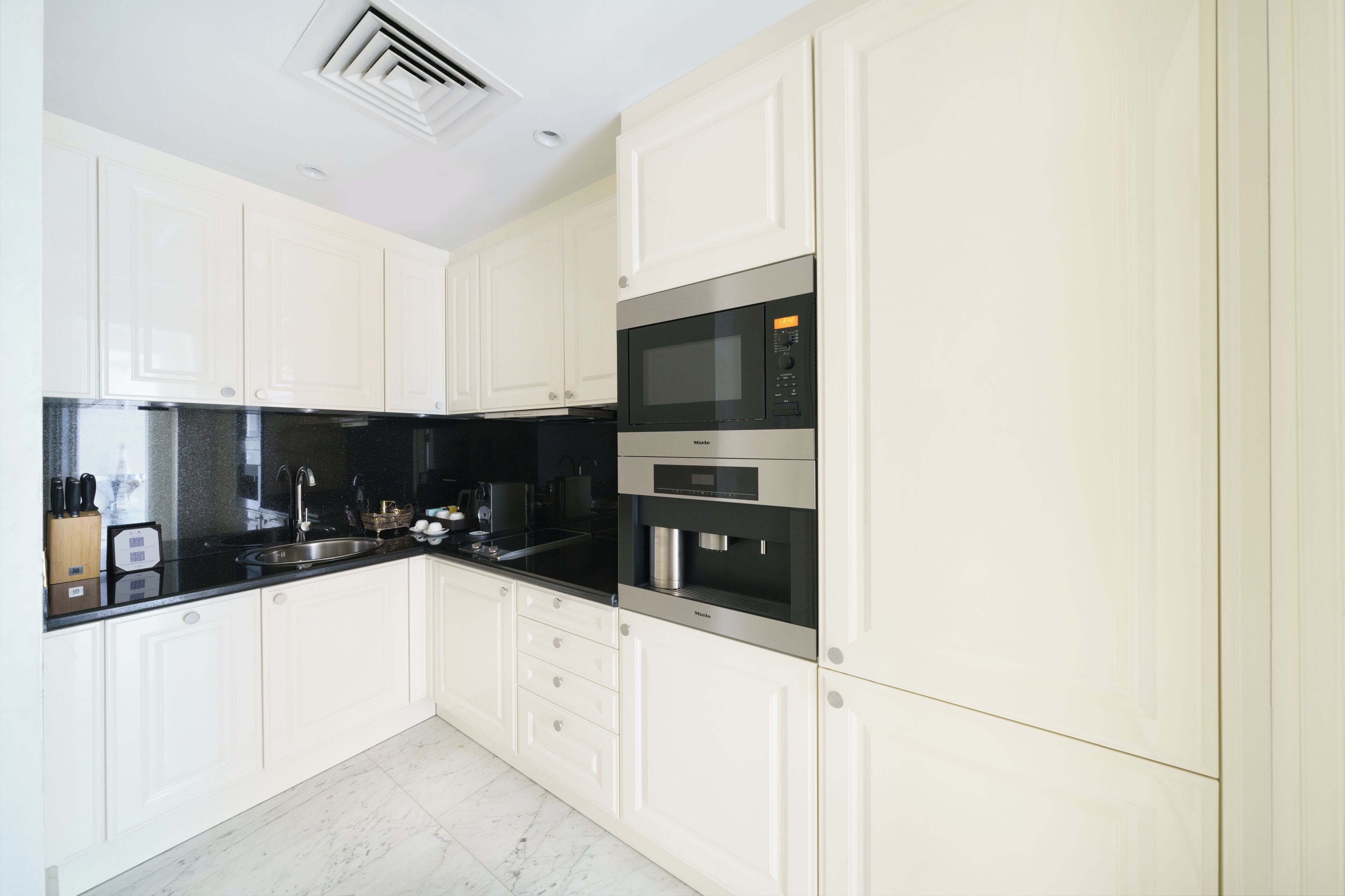Una cocina moderna con armarios blancos, encimera negra y electrodomésticos de acero inoxidable, incluyendo un microondas y un horno.