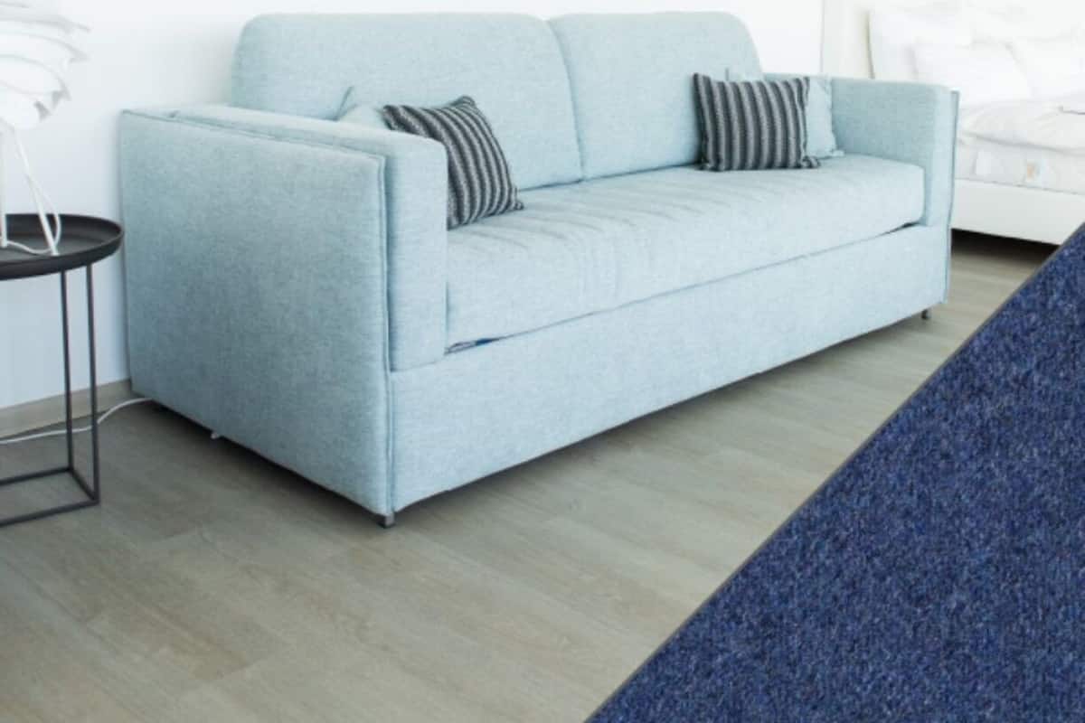Ein hellblaues Sofa mit zwei Kissen, ein kleiner schwarzer Beistelltisch und ein weißer Nachttisch in einem modernen Zimmer mit hellem Holzboden.