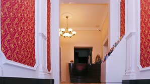 Een statige hal met decoratief rood behang, een kroonluchter en een trap naar een andere kamer.