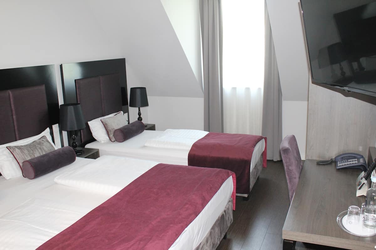 Ein Hotelzimmer mit zwei Betten, einem Schreibtisch mit Telefon und Brillen sowie einem Fernseher an der Wand.