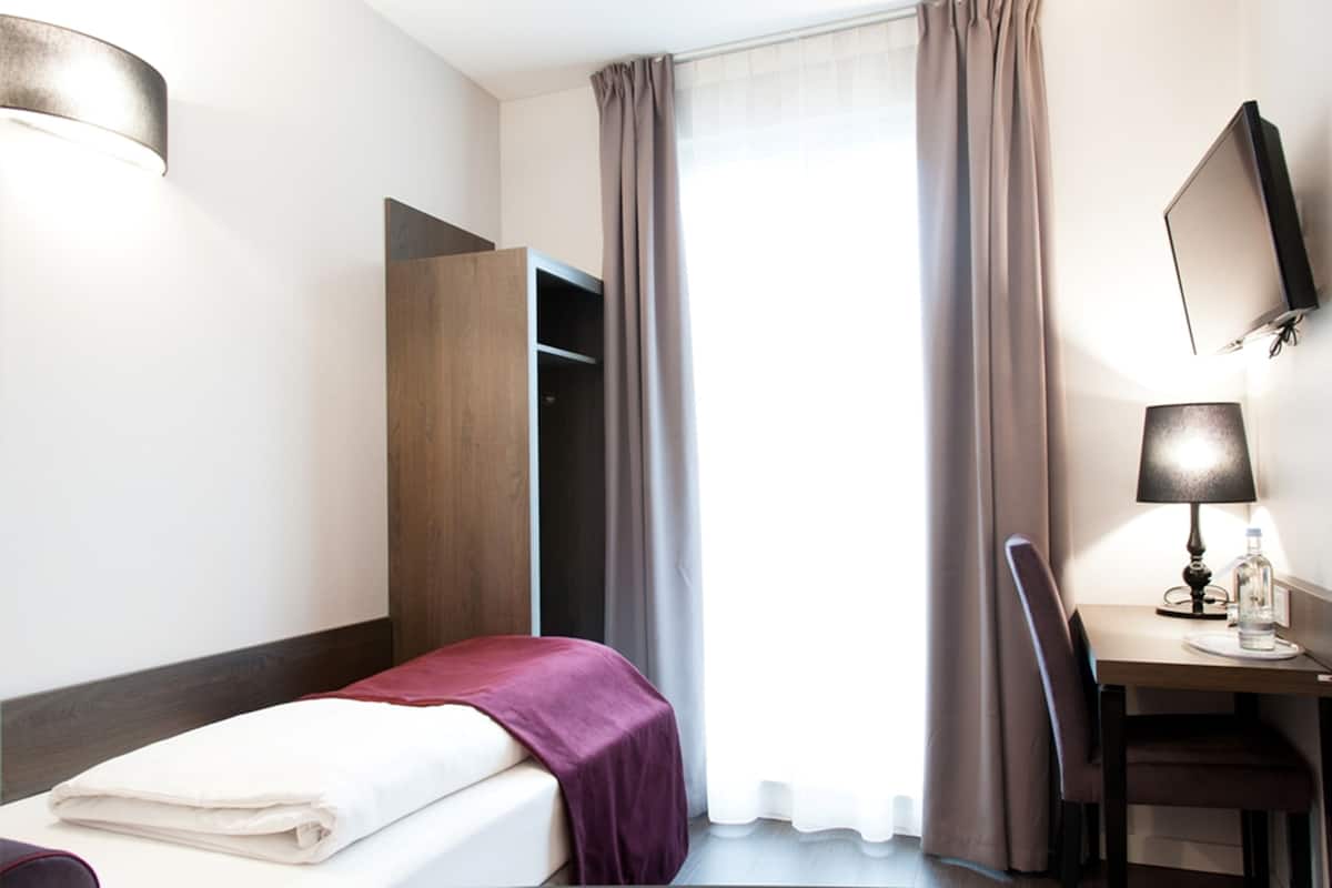 Ein Hotelzimmer mit Bett, Schreibtisch, Stuhl, Kleiderschrank und einem Fenster mit Vorhängen.