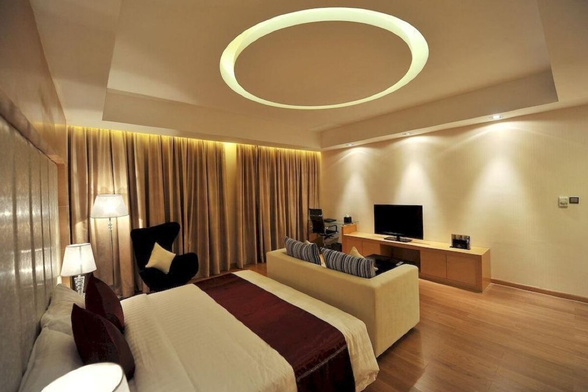 Une chambre d’hôtel moderne avec un grand lit, un bureau, une chaise, une télévision et un luminaire circulaire au plafond.