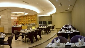 Un restaurant avec des tables rondes, des chaises sombres et une colonne centrale.