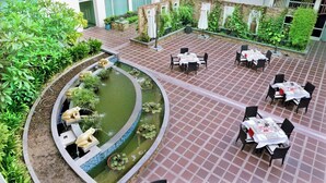 Un espace de restauration en plein air, aménagé avec des tables et des chaises, entouré de verdure et agrémenté d’un petit étang décoratif.