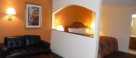 Habitación de hotel con sofá de cuero negro, una mesita de madera, un separador blanco y una cama con colcha estampada.