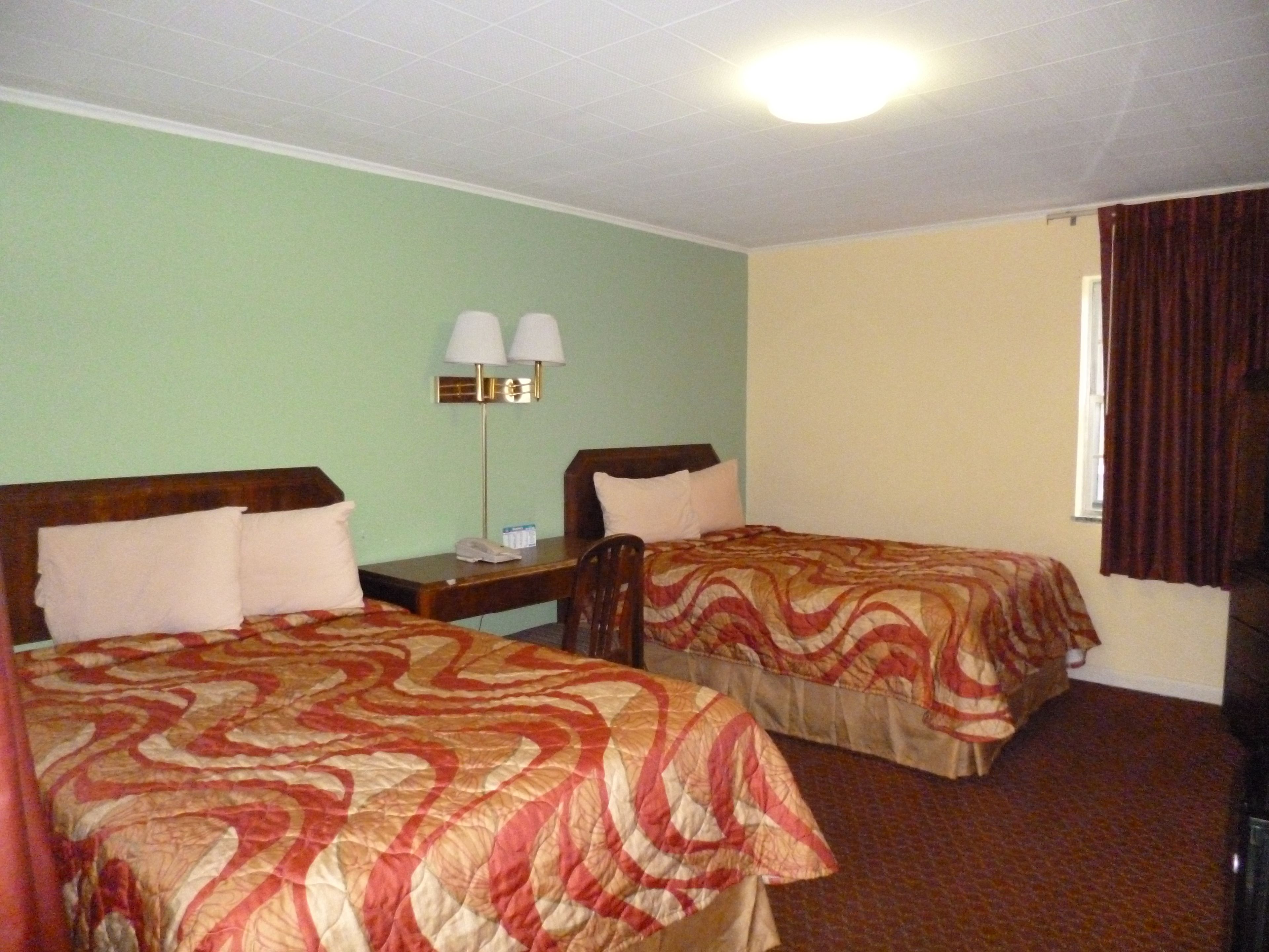 Habitación de hotel con dos camas individuales, una mesita de noche con lámpara y una ventana con cortinas.