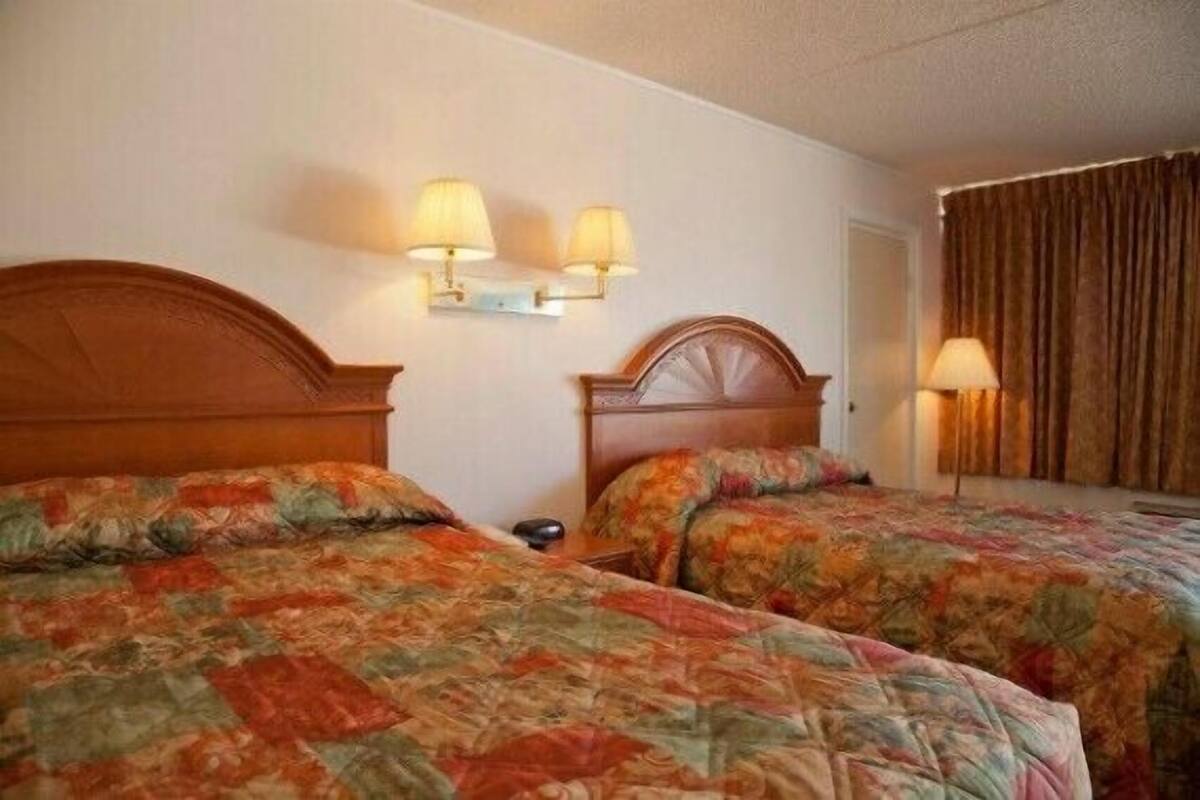 A hotel room with two beds, each with a floral-patterned bedspread, a wooden headboard, and two wall-mounted lamps.