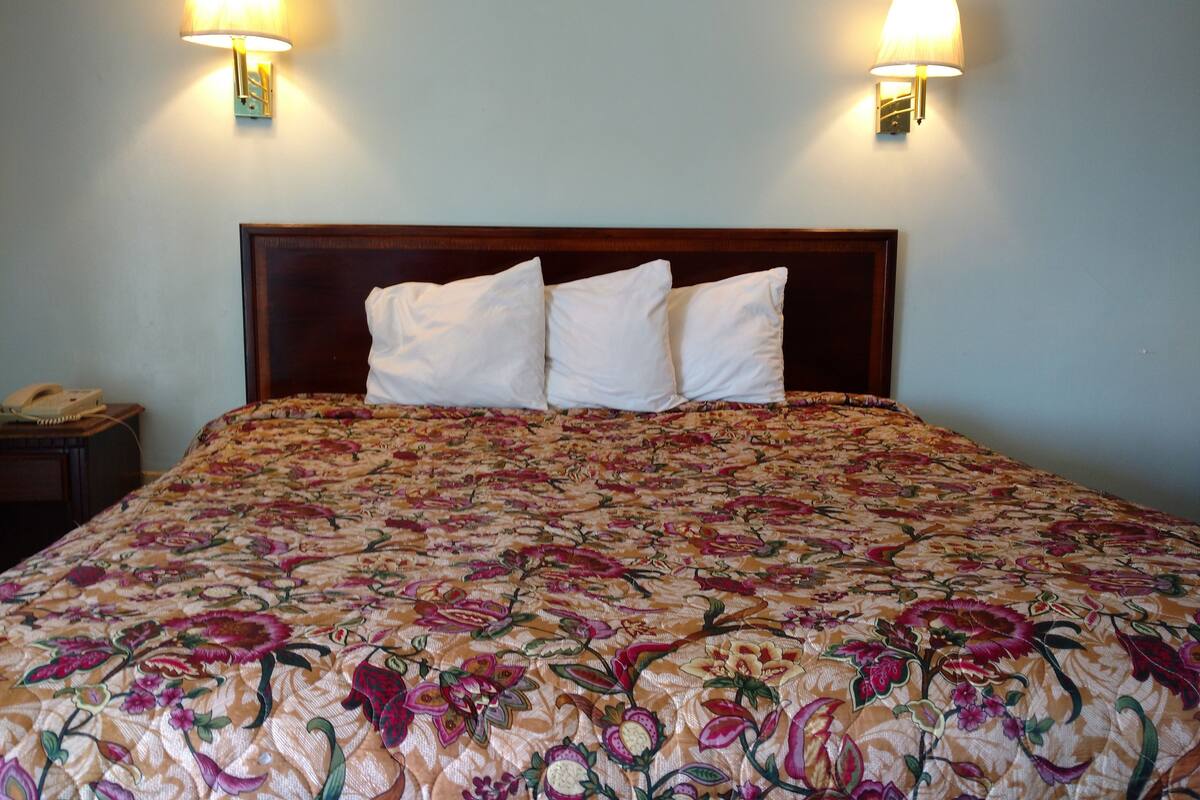 A bed with a floral bedspread, two wall-mounted lamps, and a wooden headboard.