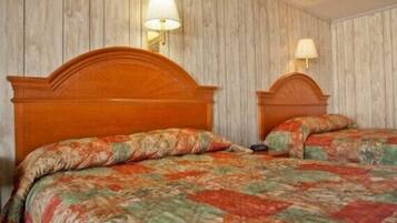 Cama doble con edredón estampado de flores en una habitación con paneles de madera y dos lámparas fijadas a la pared.