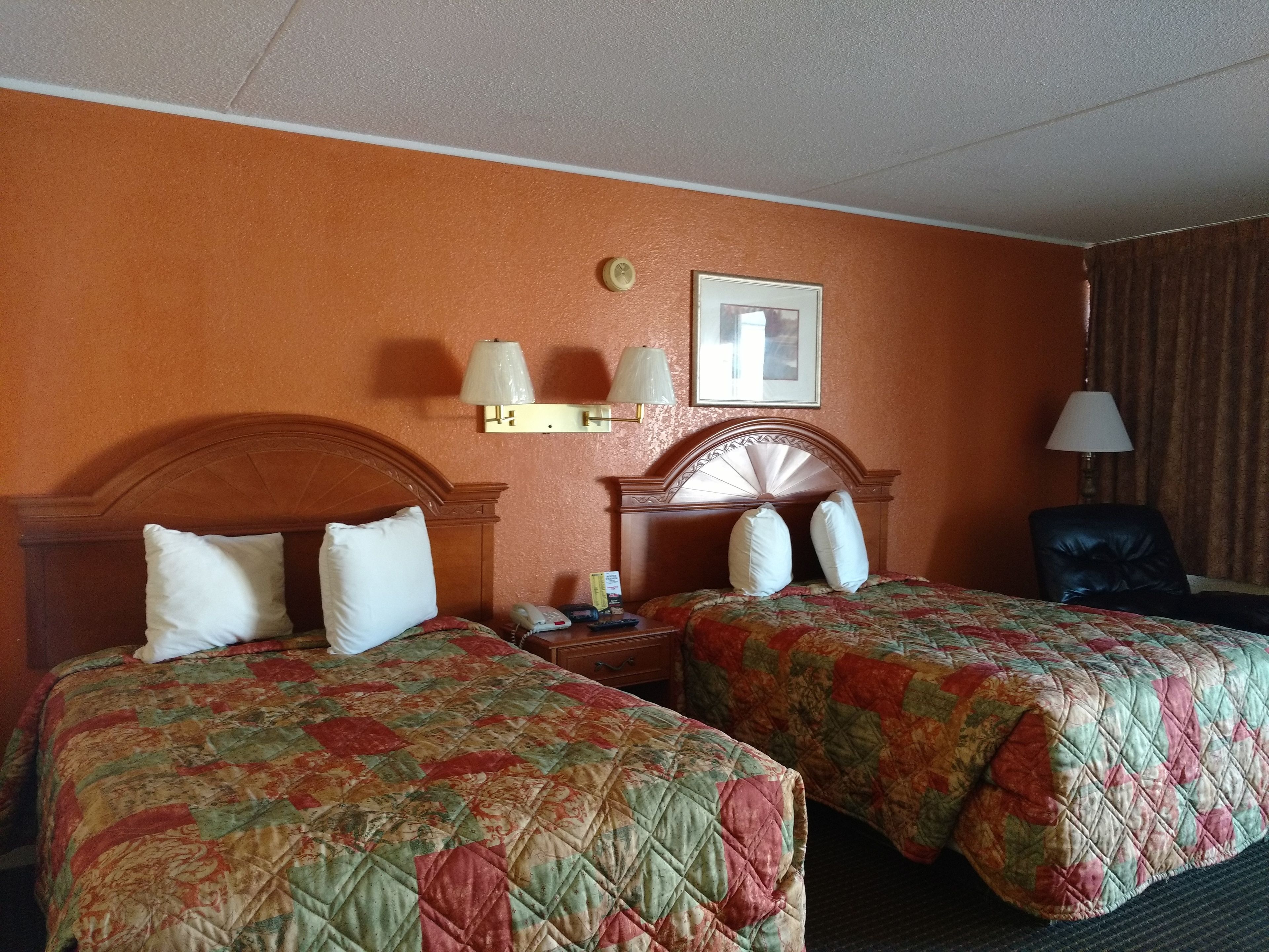 Habitación de hotel con dos camas, cabecero de madera, mesita de noche, lámpara y un cuadro en la pared.
