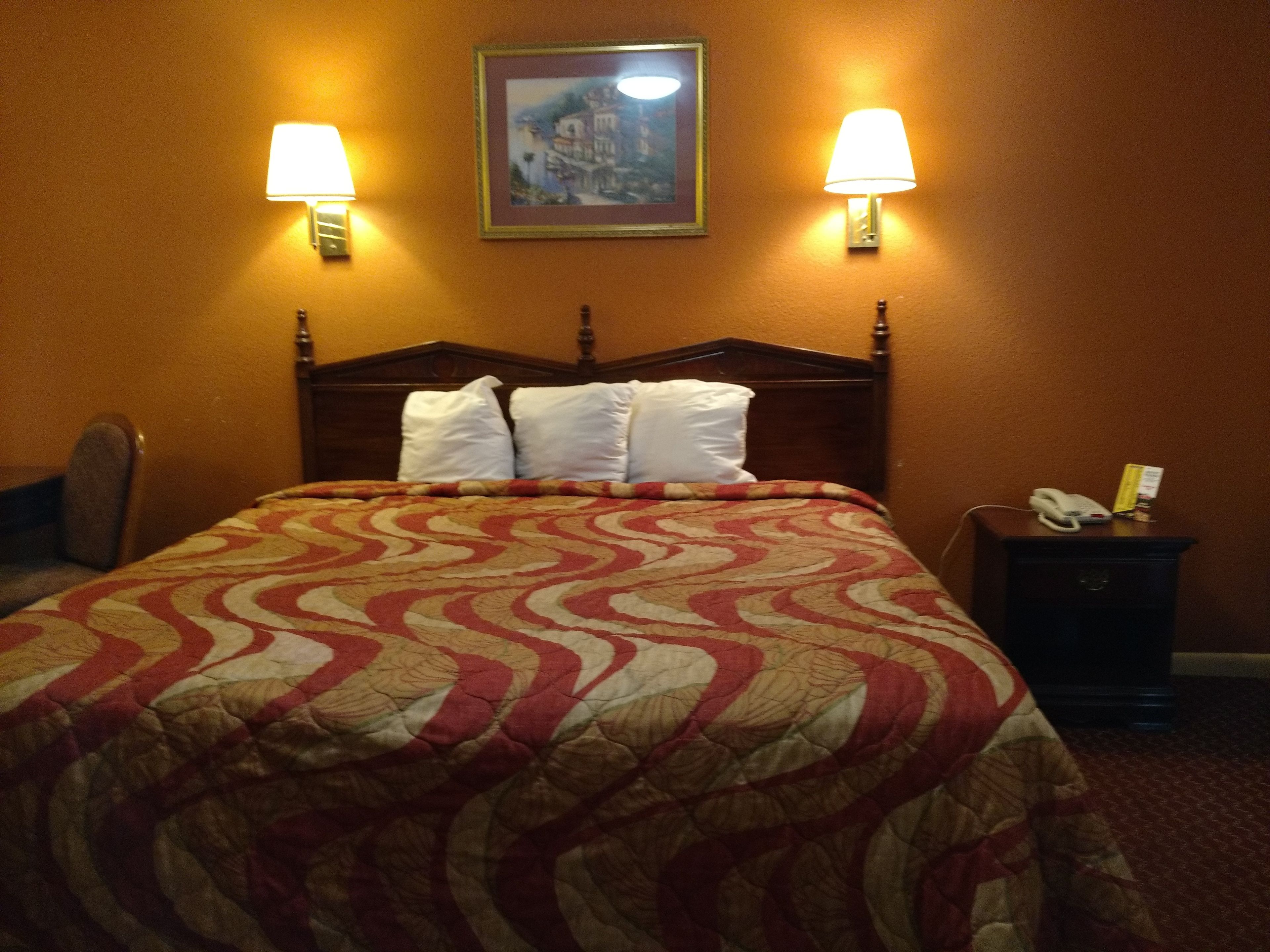 Una habitación de hotel con una cama grande, dos lámparas de pared, un cuadro sobre la cama y una mesita de noche con un teléfono y una caja.
